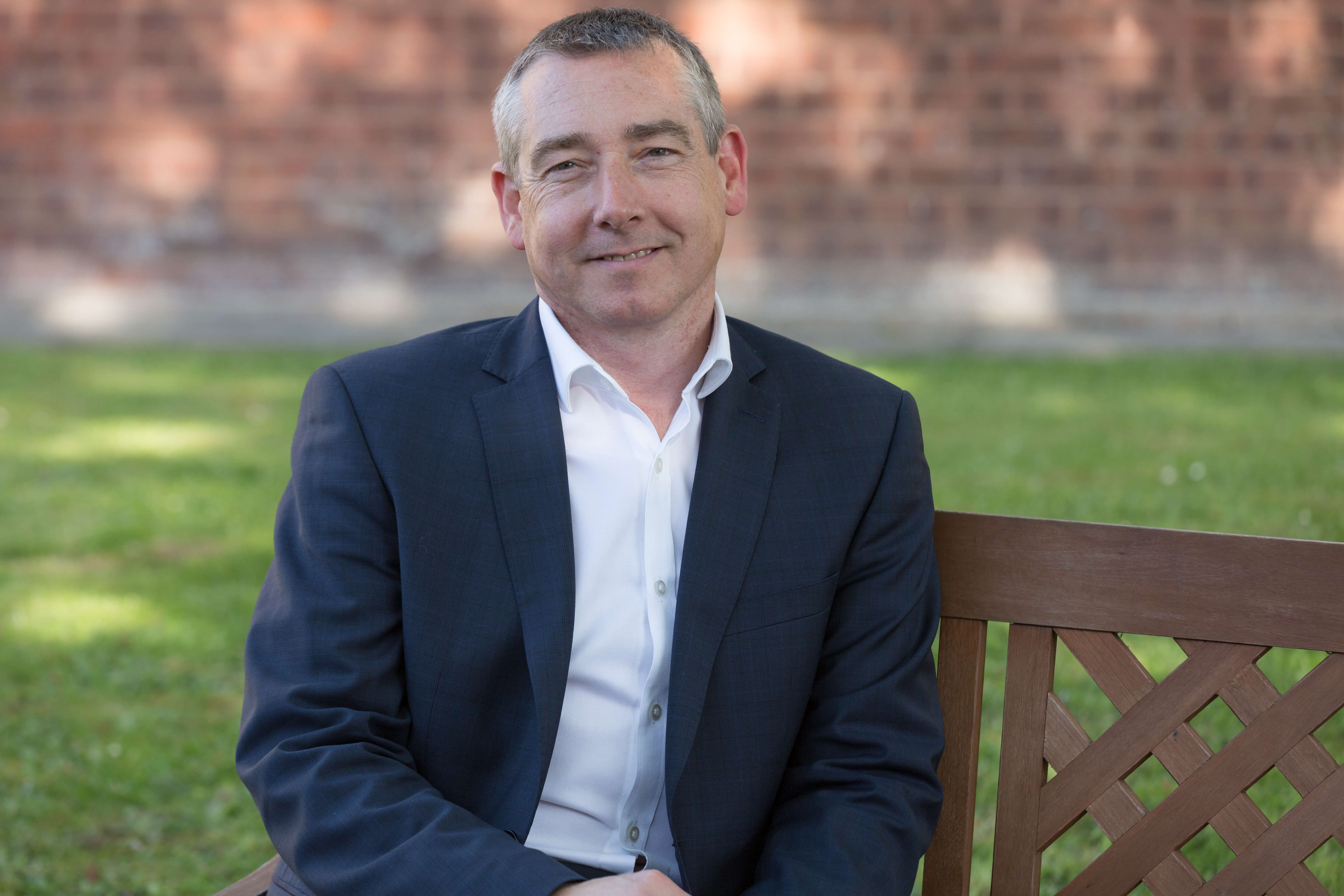 Man in suit sitting on a wooden bench in a garden