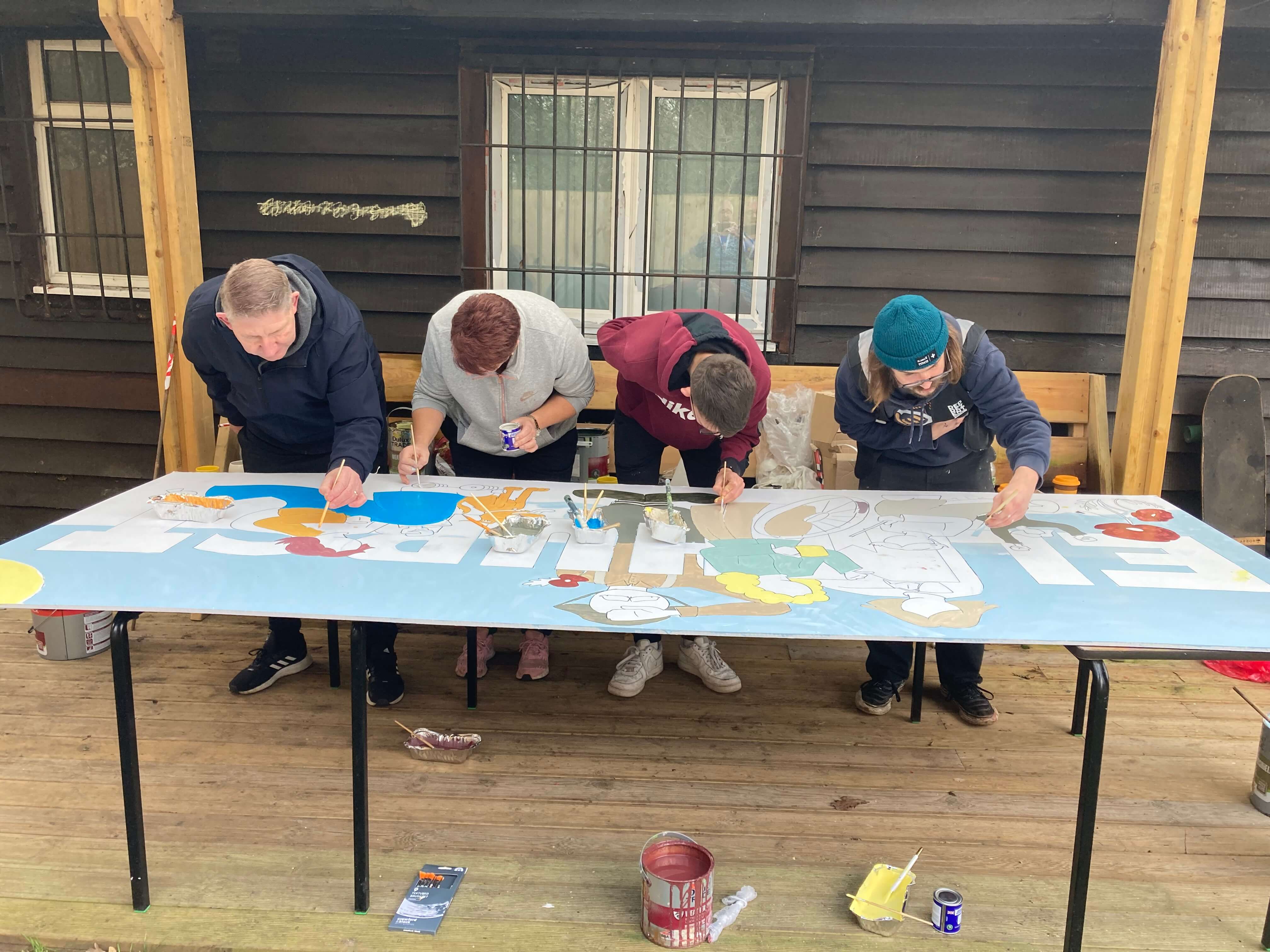 four people leaning over a table painting a mural