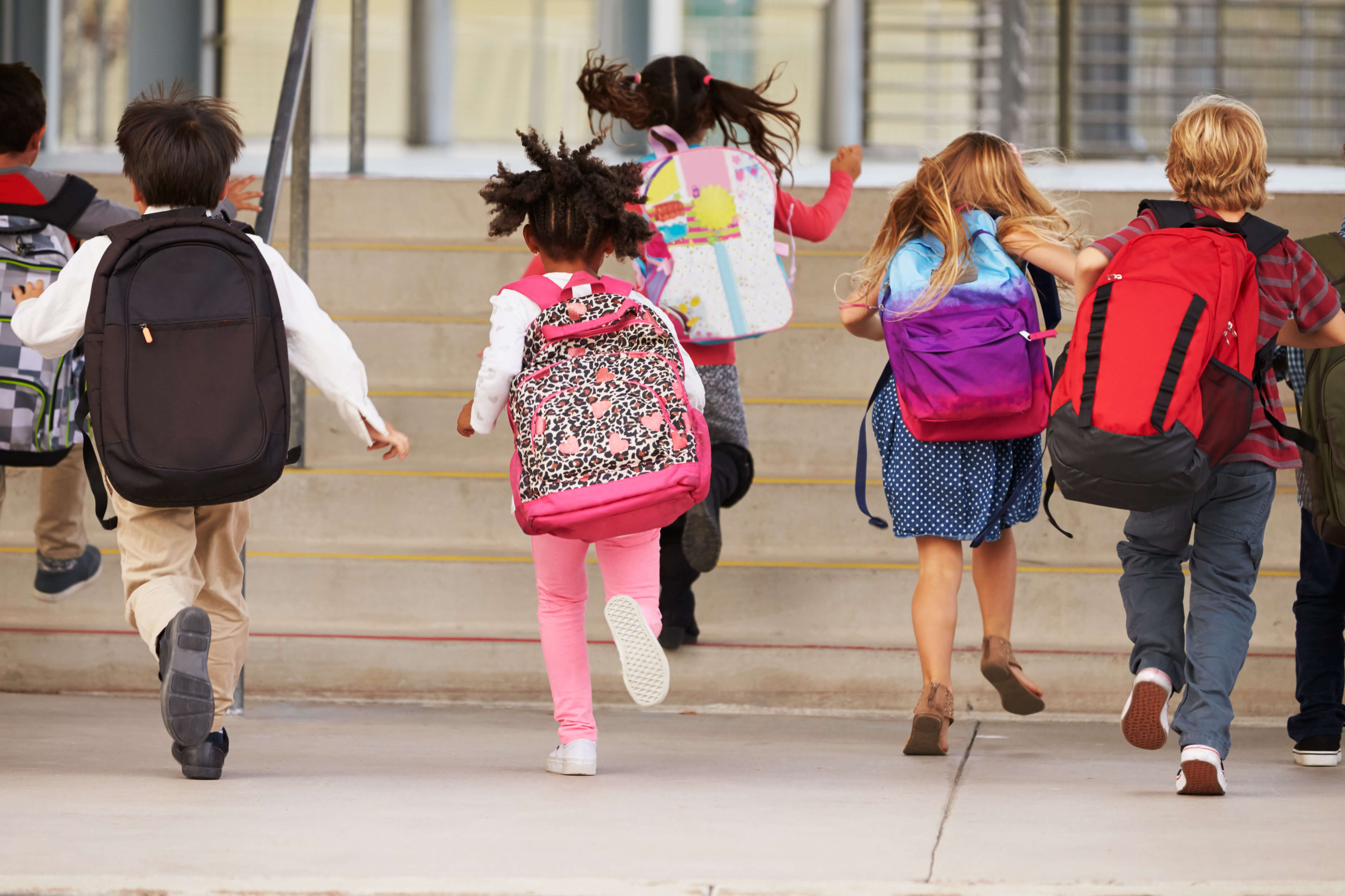 children running in to school with their backpacks