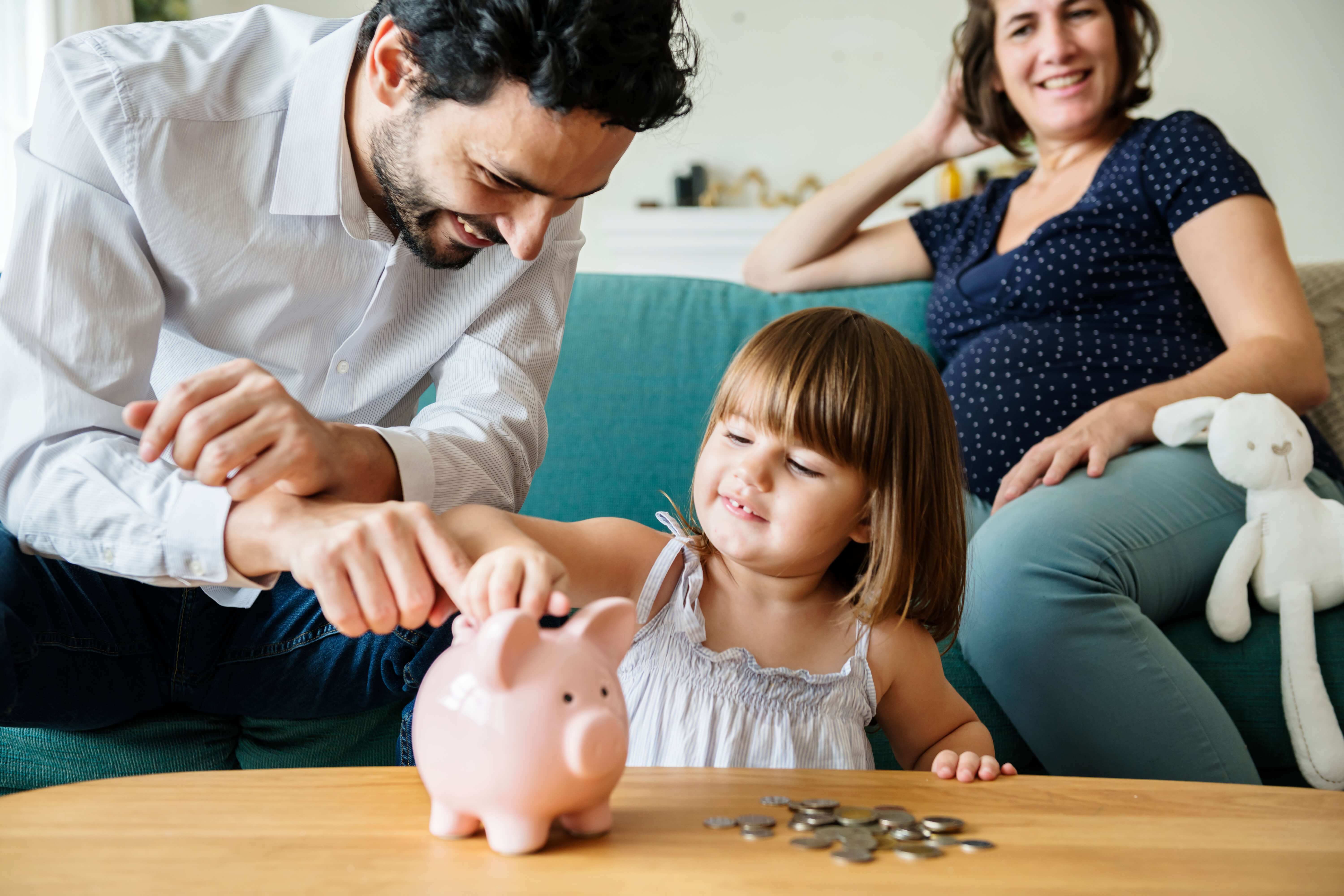 Father helping his daughter putting coins into a piggy bank