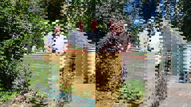 three men and two women standing in a garden in front of a planter box in the sunshine smiling holding gardening tools with a small glasshouse behind them three men and two women standing in a garden in front of a planter box in the sunshine smiling holding gardening tools with a small glasshouse behind them