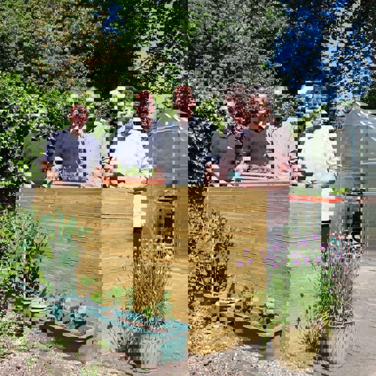 three men and two women standing in a garden in front of a planter box in the sunshine smiling holding gardening tools with a small glasshouse behind them three men and two women standing in a garden in front of a planter box in the sunshine smiling holding gardening tools with a small glasshouse behind them