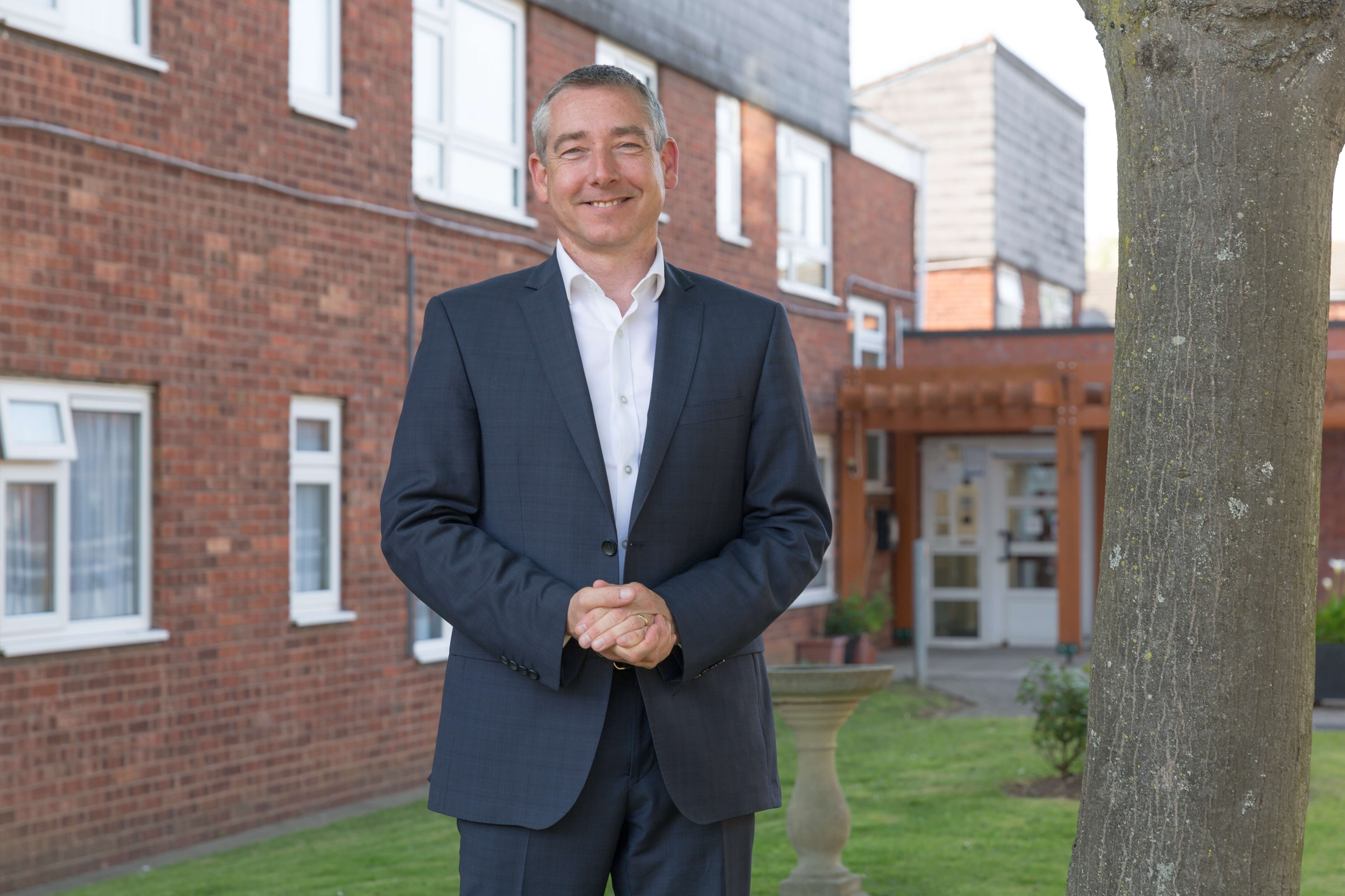 Man standing on a lawn in front of a bricked building