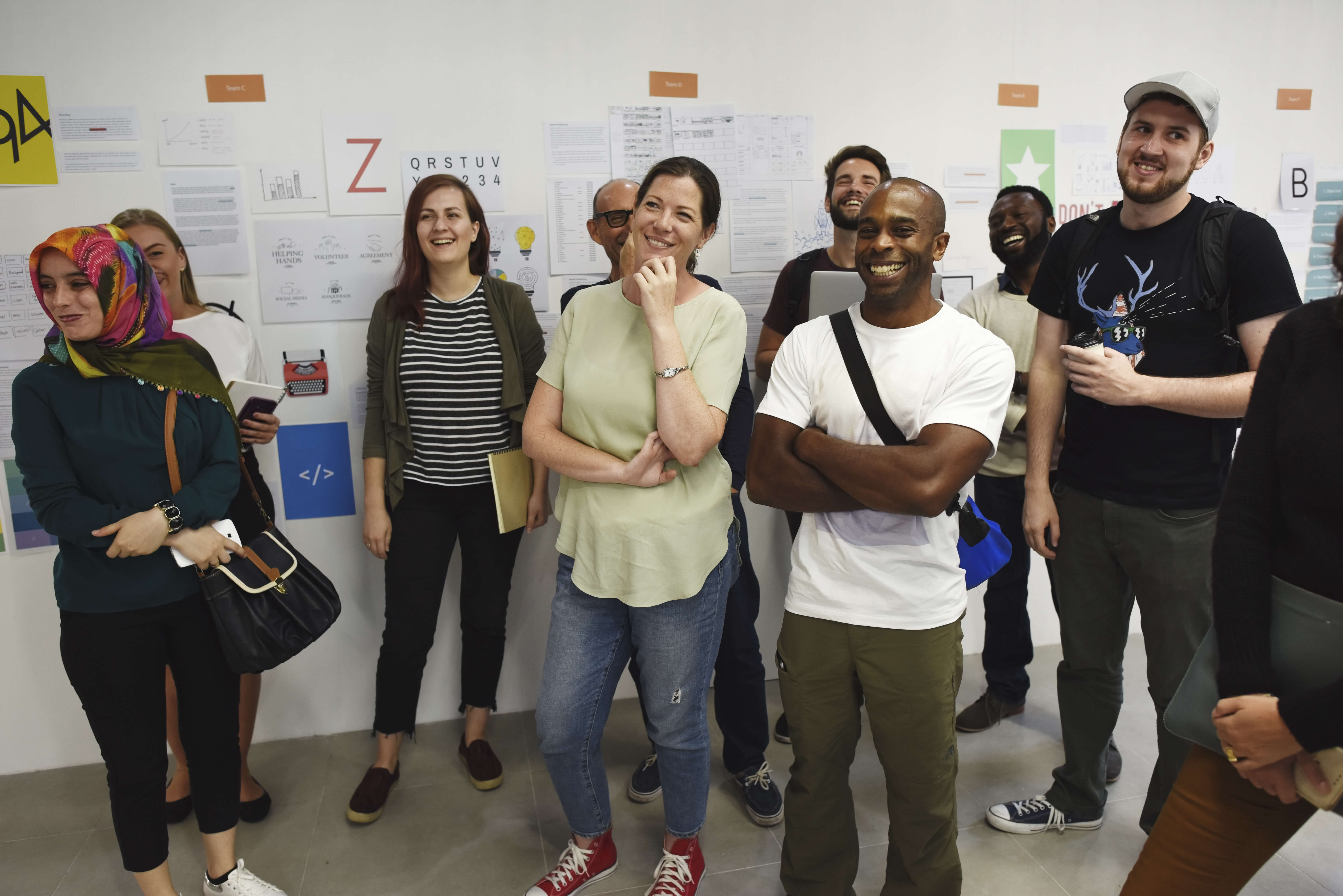 Group of people standing and smiling whilst listening to someone talk