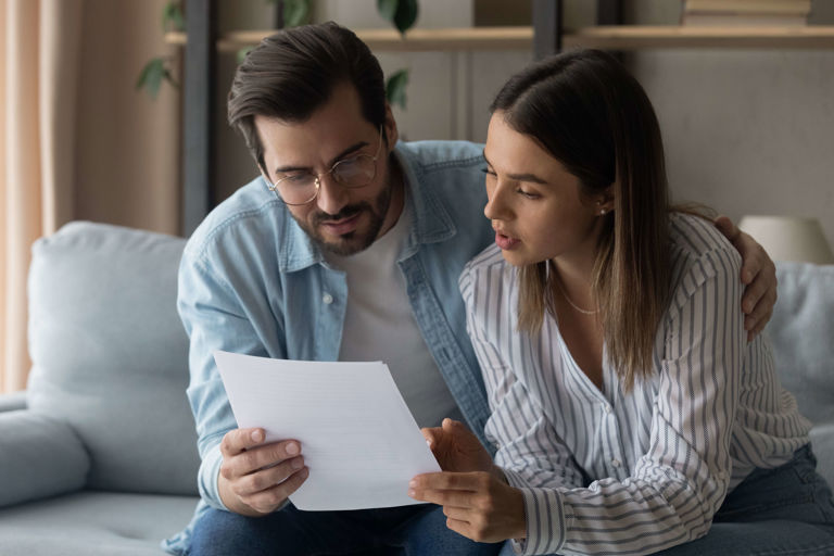 couple sitting on couch looking at a letter couple sitting on couch looking at a letter