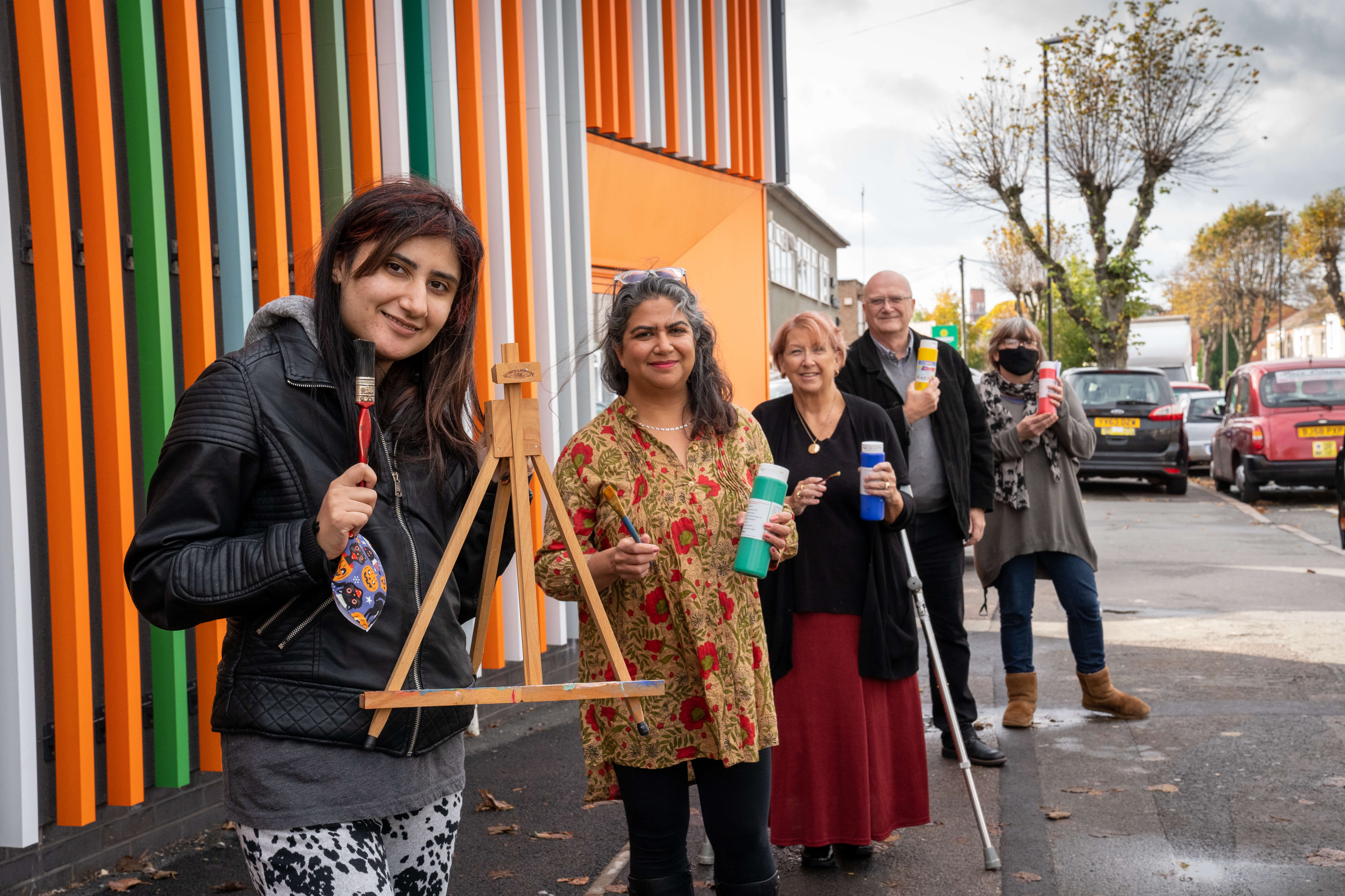 people standing outside a colourful building holding art supplies