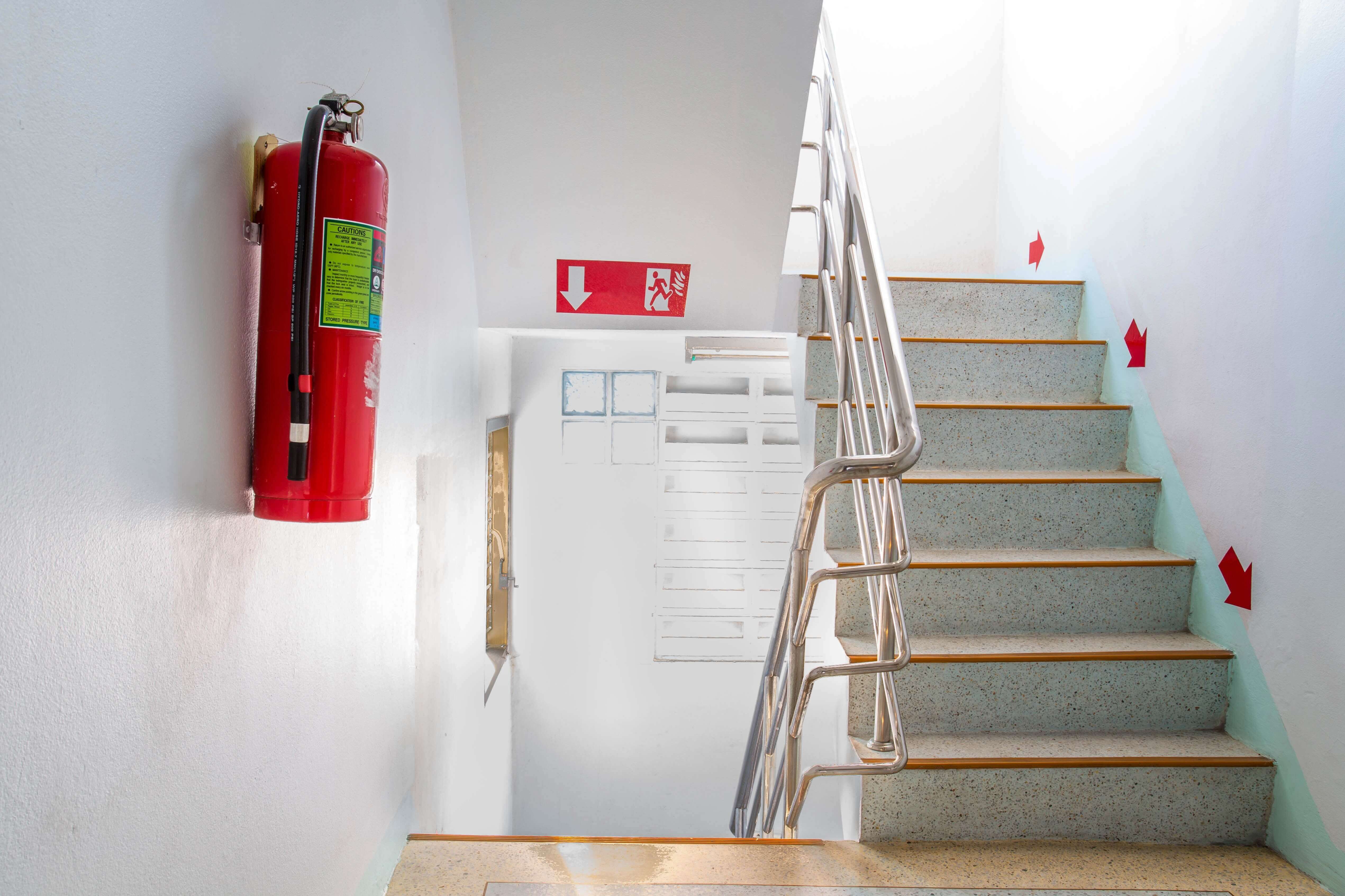 staircase with white walls leading to a eacuation door with red fire extinguisher on the wall