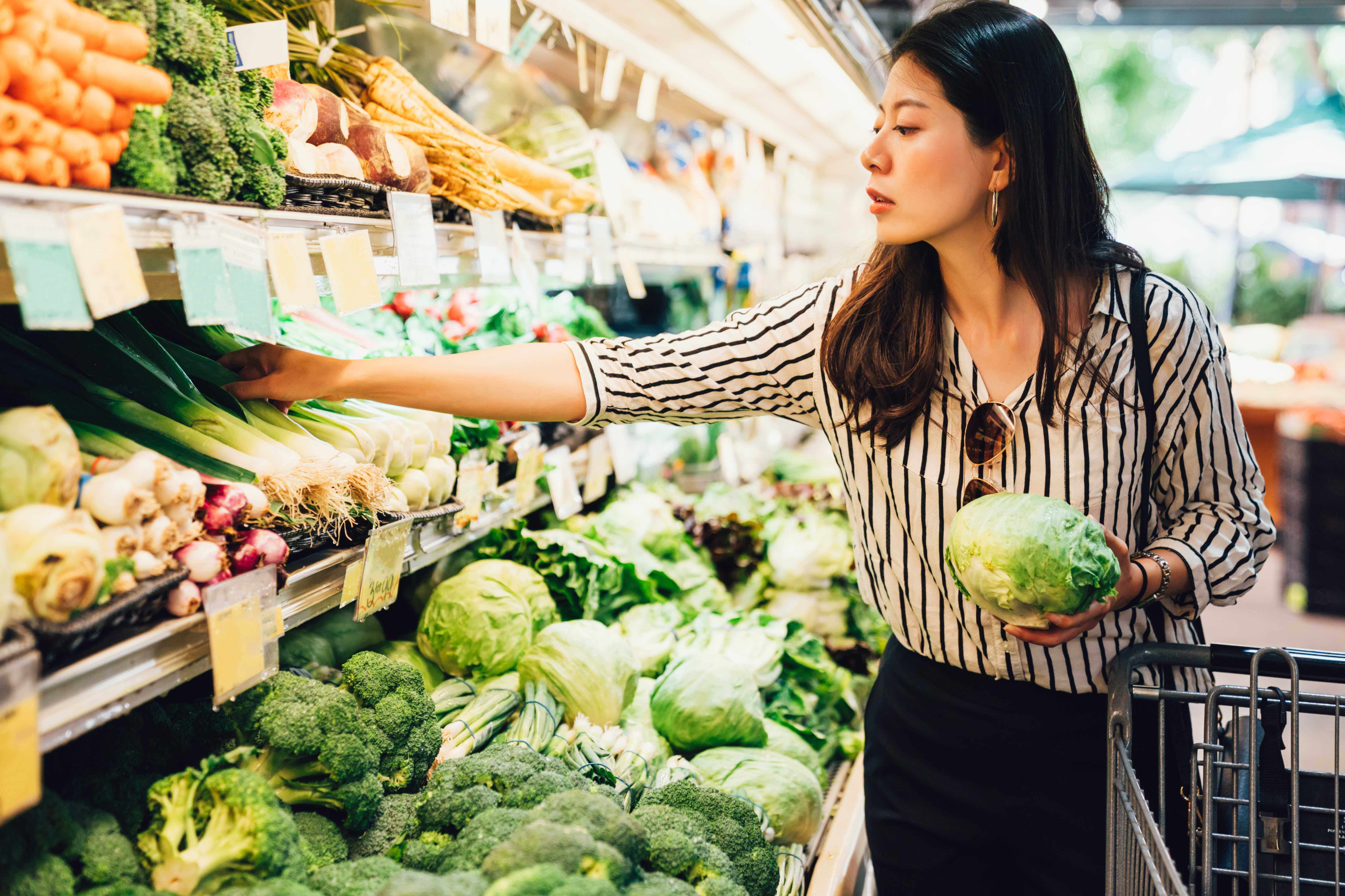 Chinese lady holding a vegetable in front of a supermarket fridge