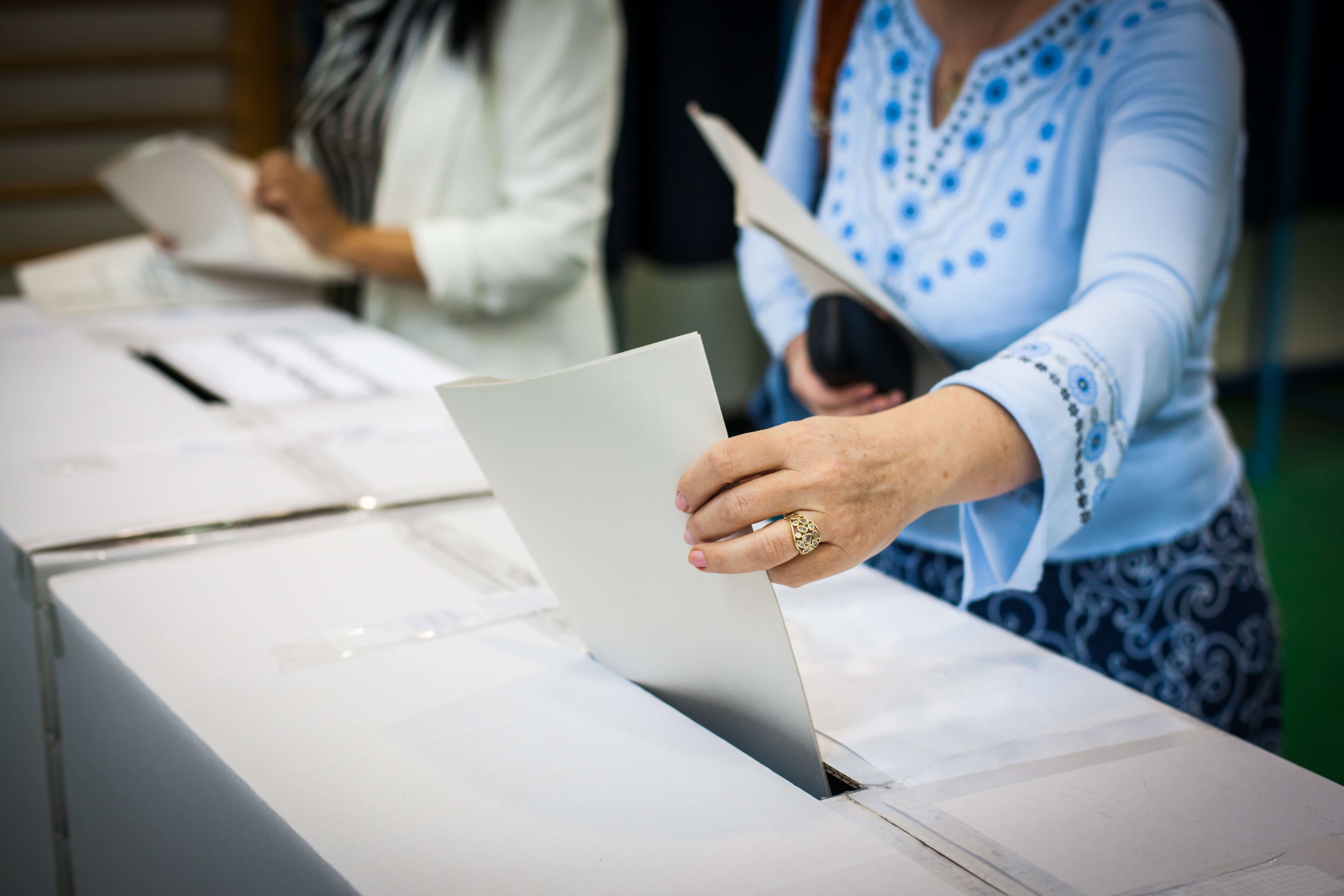 lady in blue shirt putting her vote in a voting box
