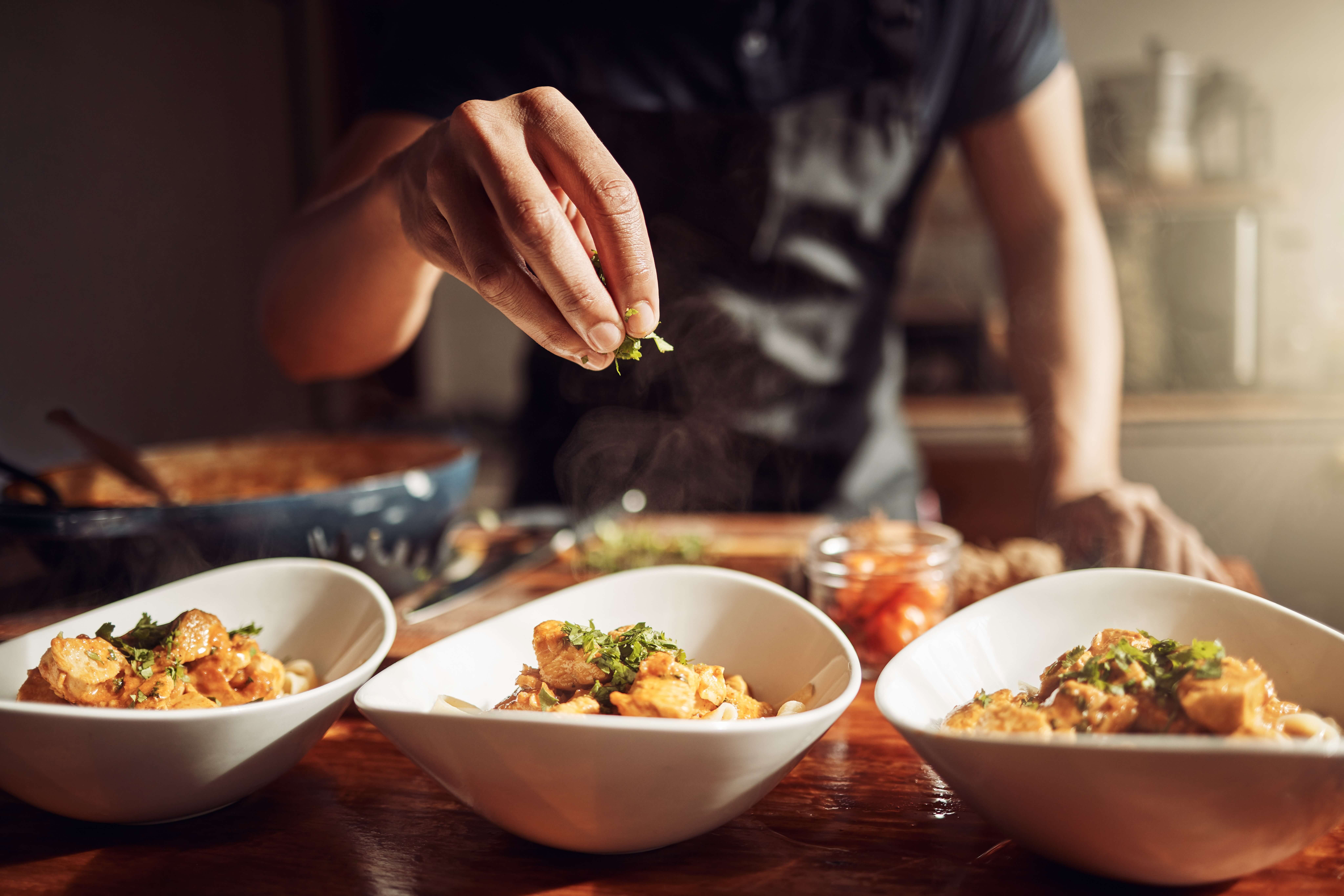 Hand drizzling herbs on food in a bowl