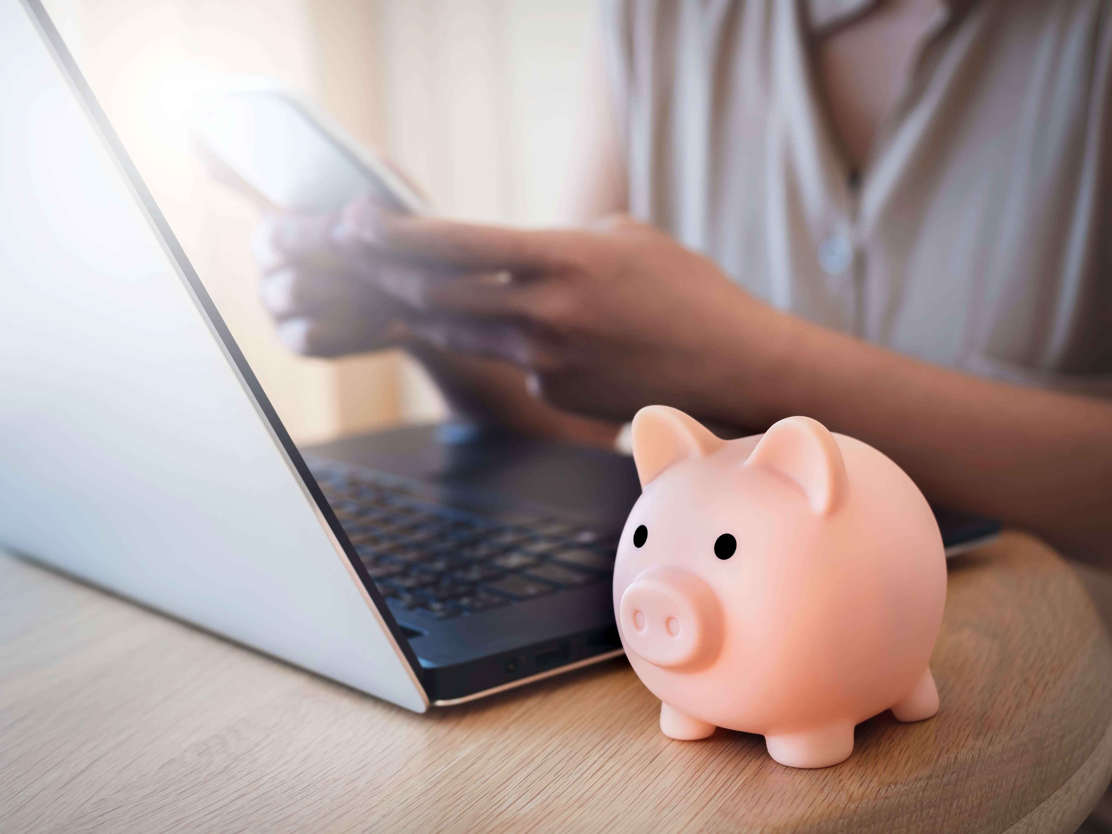 women on laptop and mobile phone with a pink piggy bank on the table