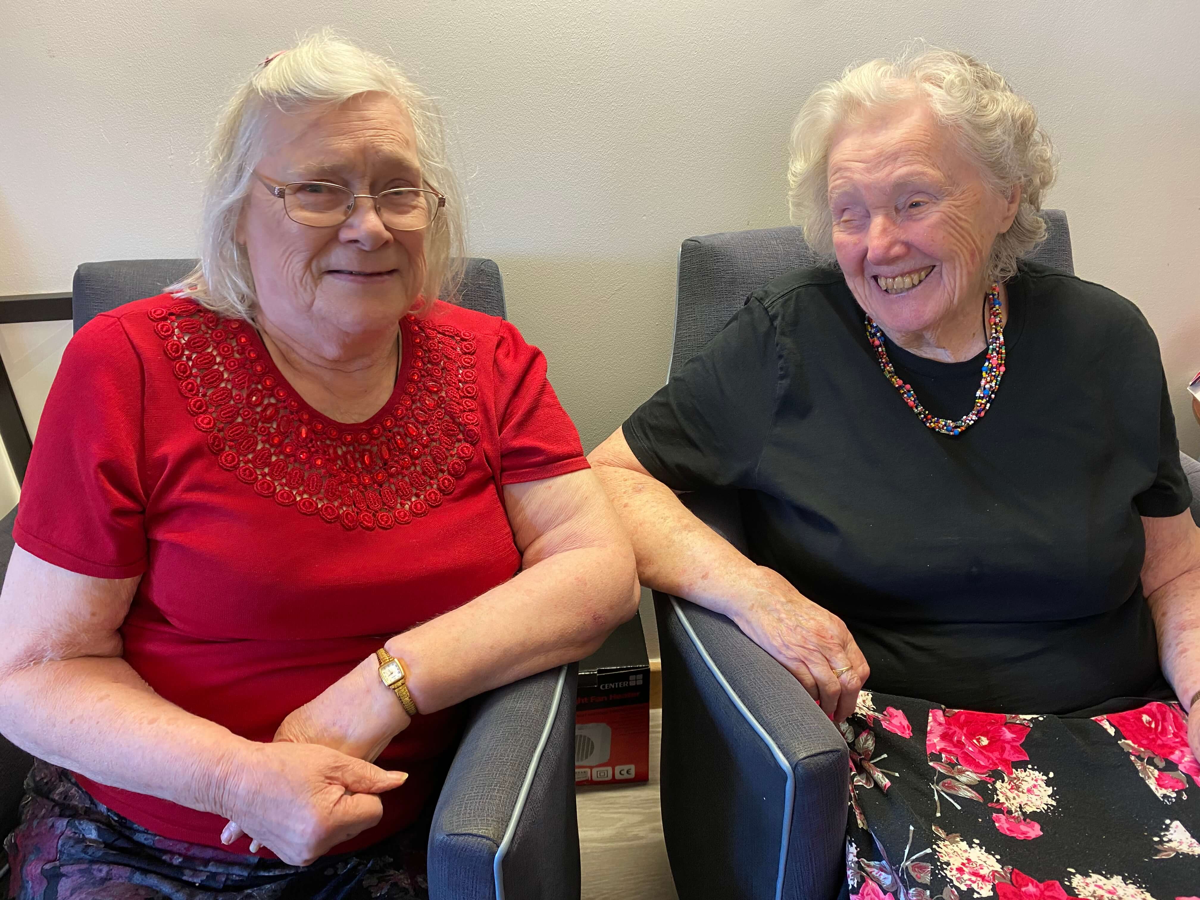 two older ladies sitting next to each other and smiling