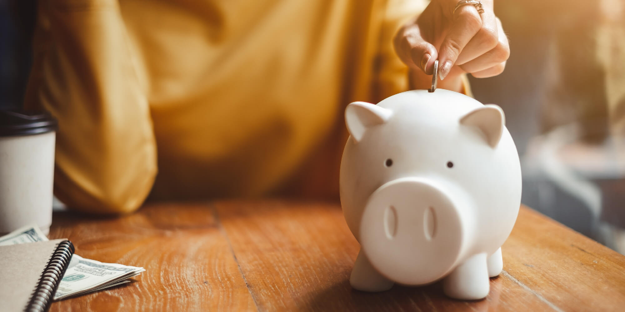person in yellow shirt putting a coin in a piggybank