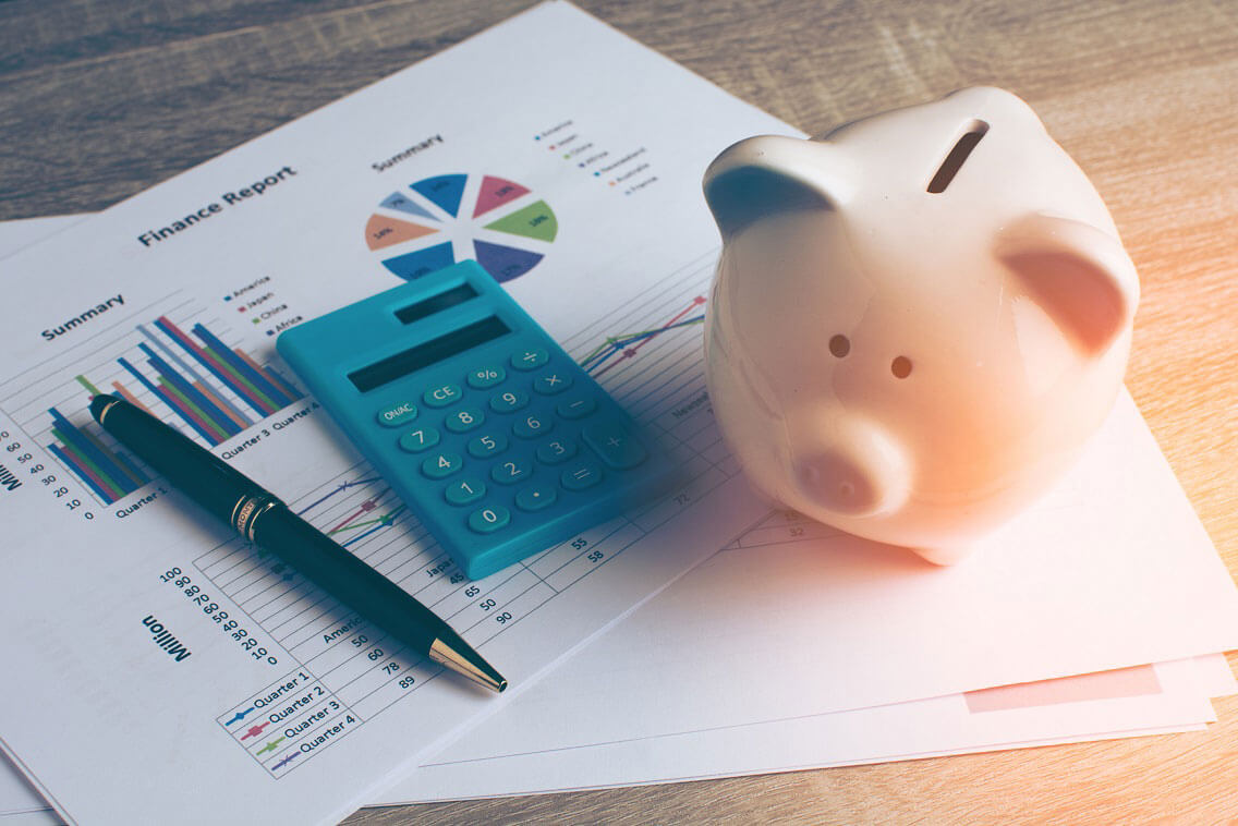 piggy bank next to a calculator and pens on pieces of paper piggy bank next to a calculator and pens on pieces of paper