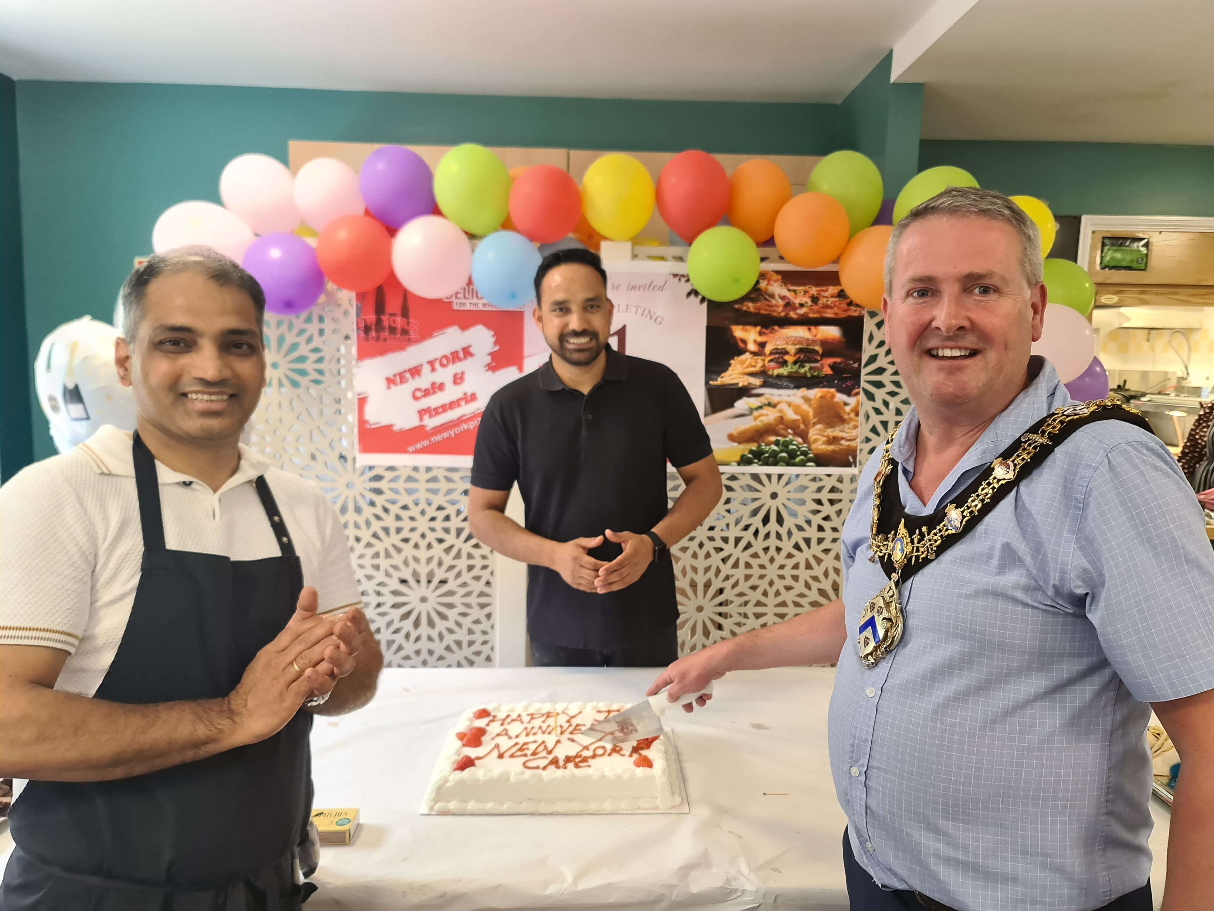 two men standing with the Stratford mayor cutting a cake two men standing with the Stratford mayor cutting a cake