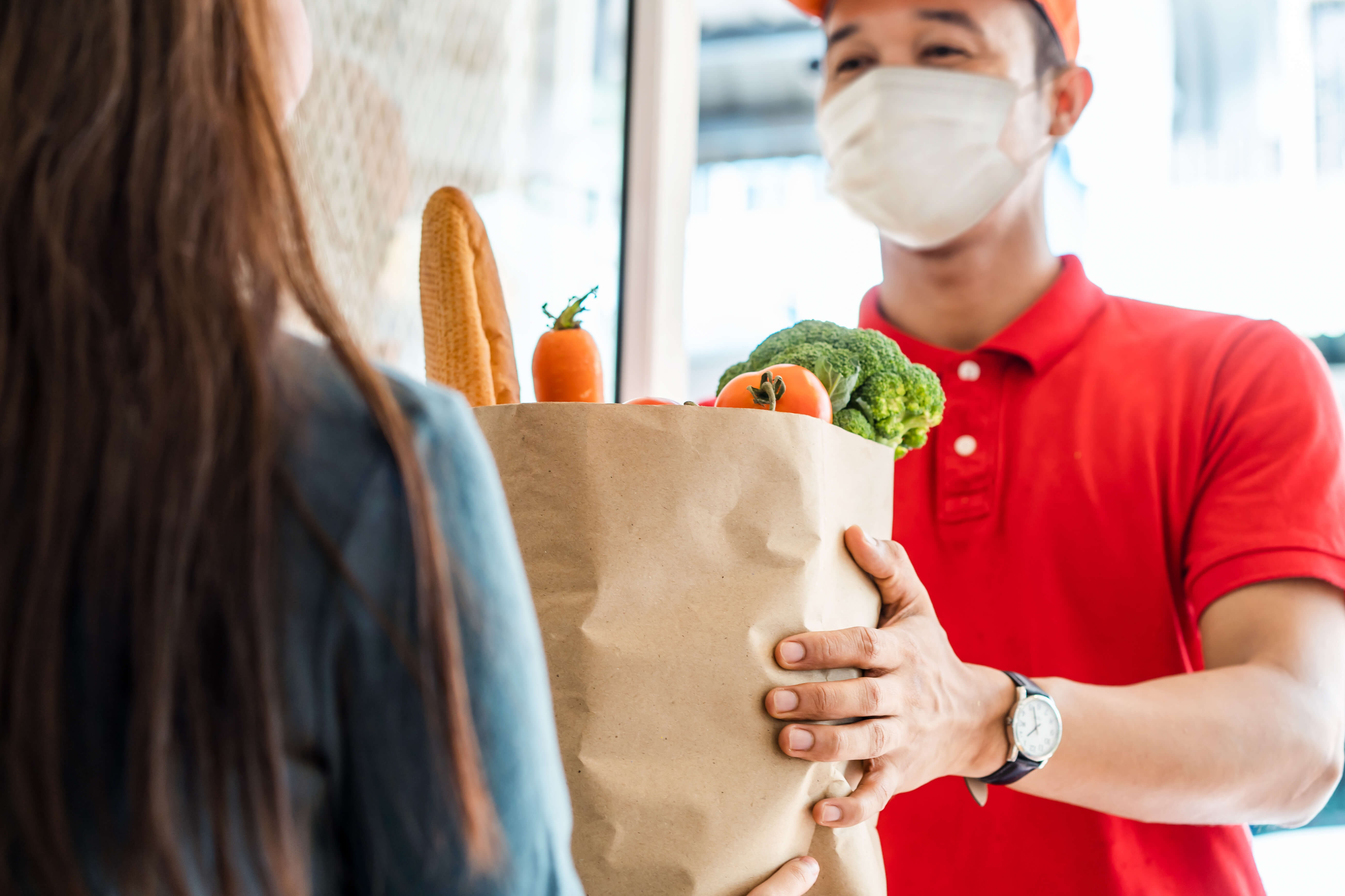 Asian man wearing a mask and delivering groceries to a lady at the door