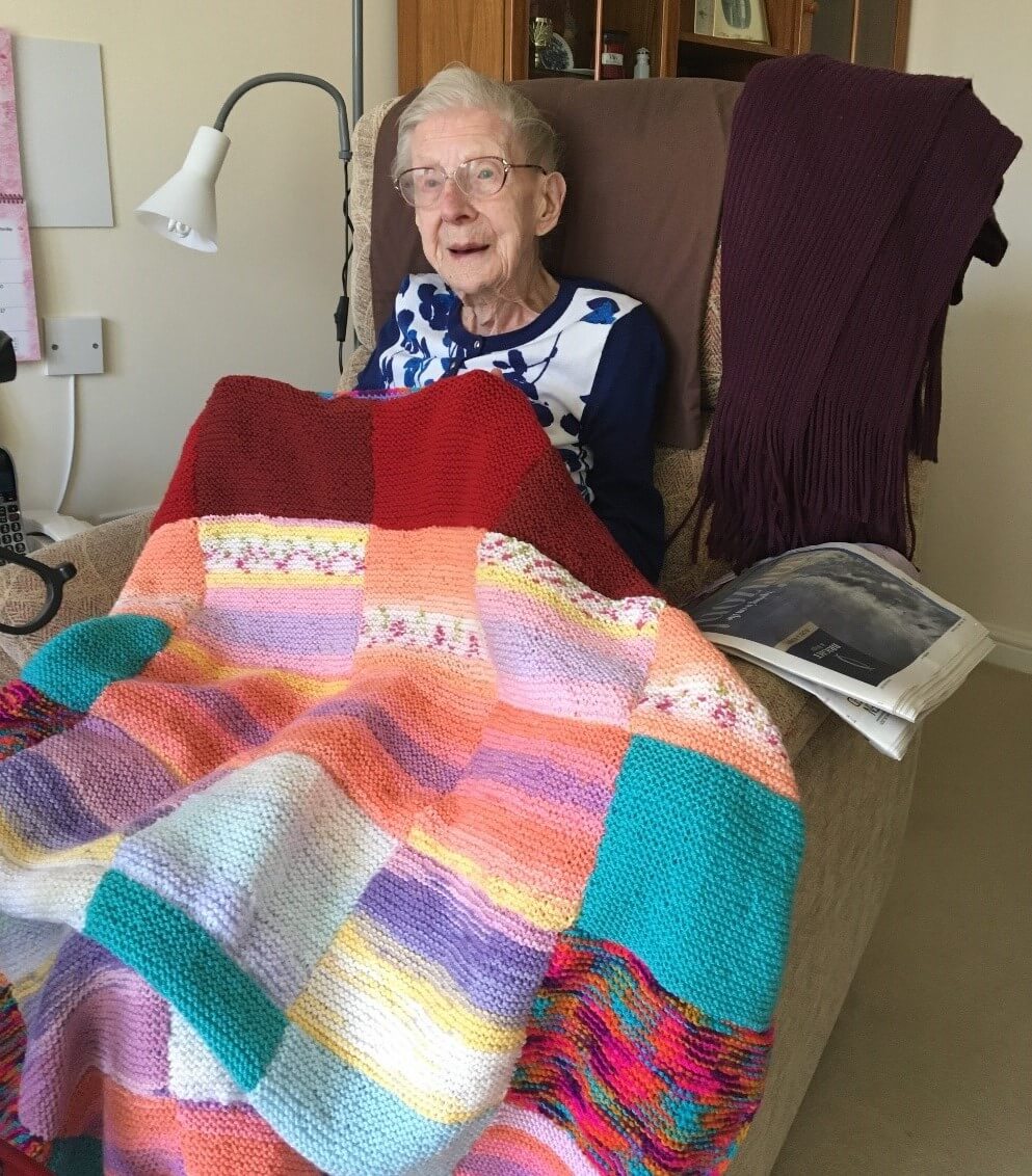 Elderly lady sitting under a colourful blanket Elderly lady sitting under a colourful blanket