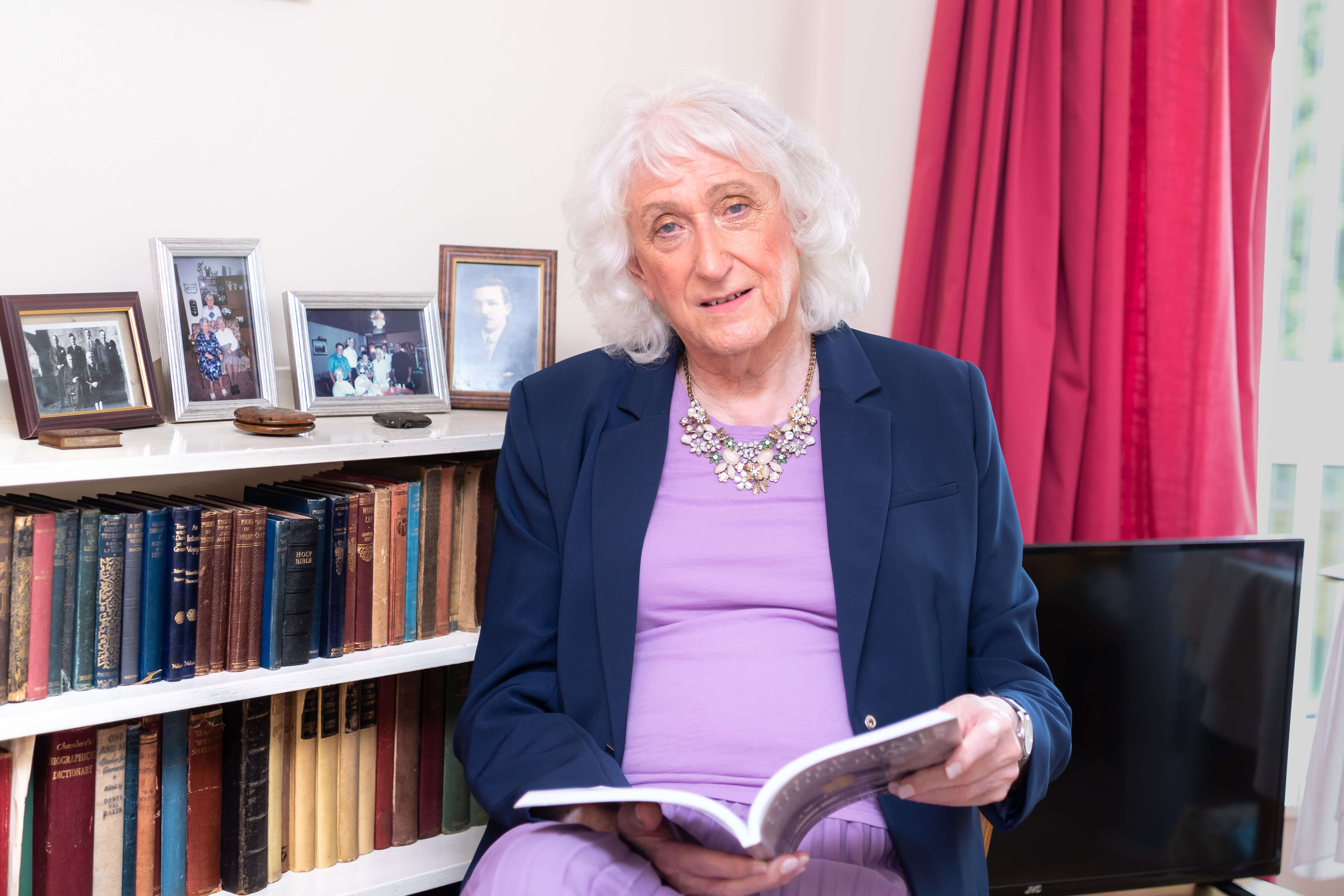 Sandra sitting in front of a bookcase reading a book