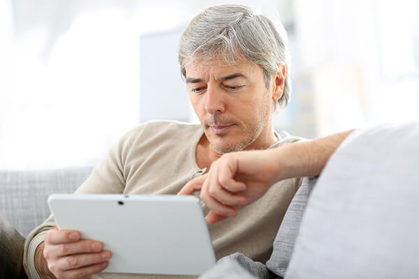 man sitting on couch typing on his tablet