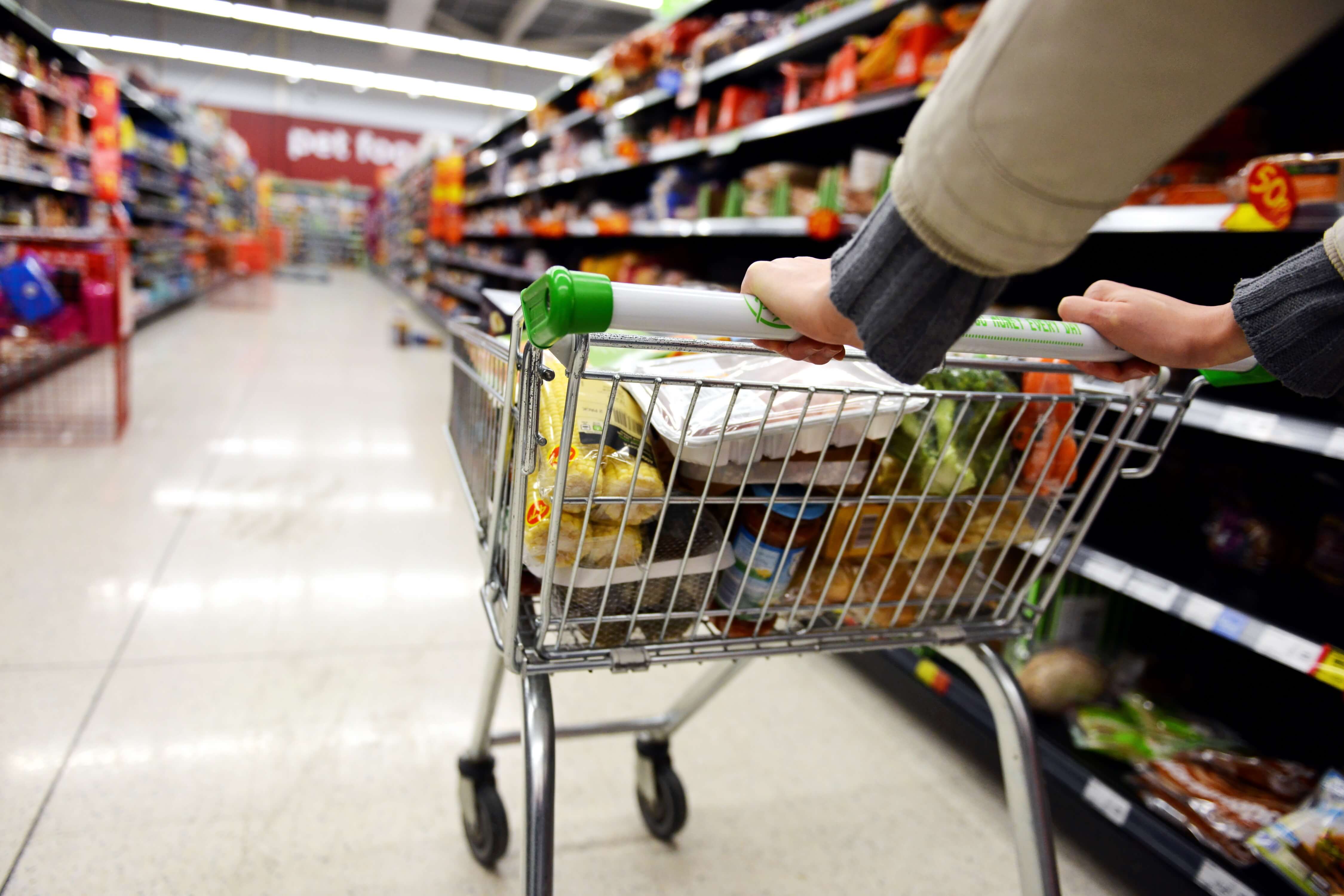 Person pushing a trolley filled with food in a supermarket aisle