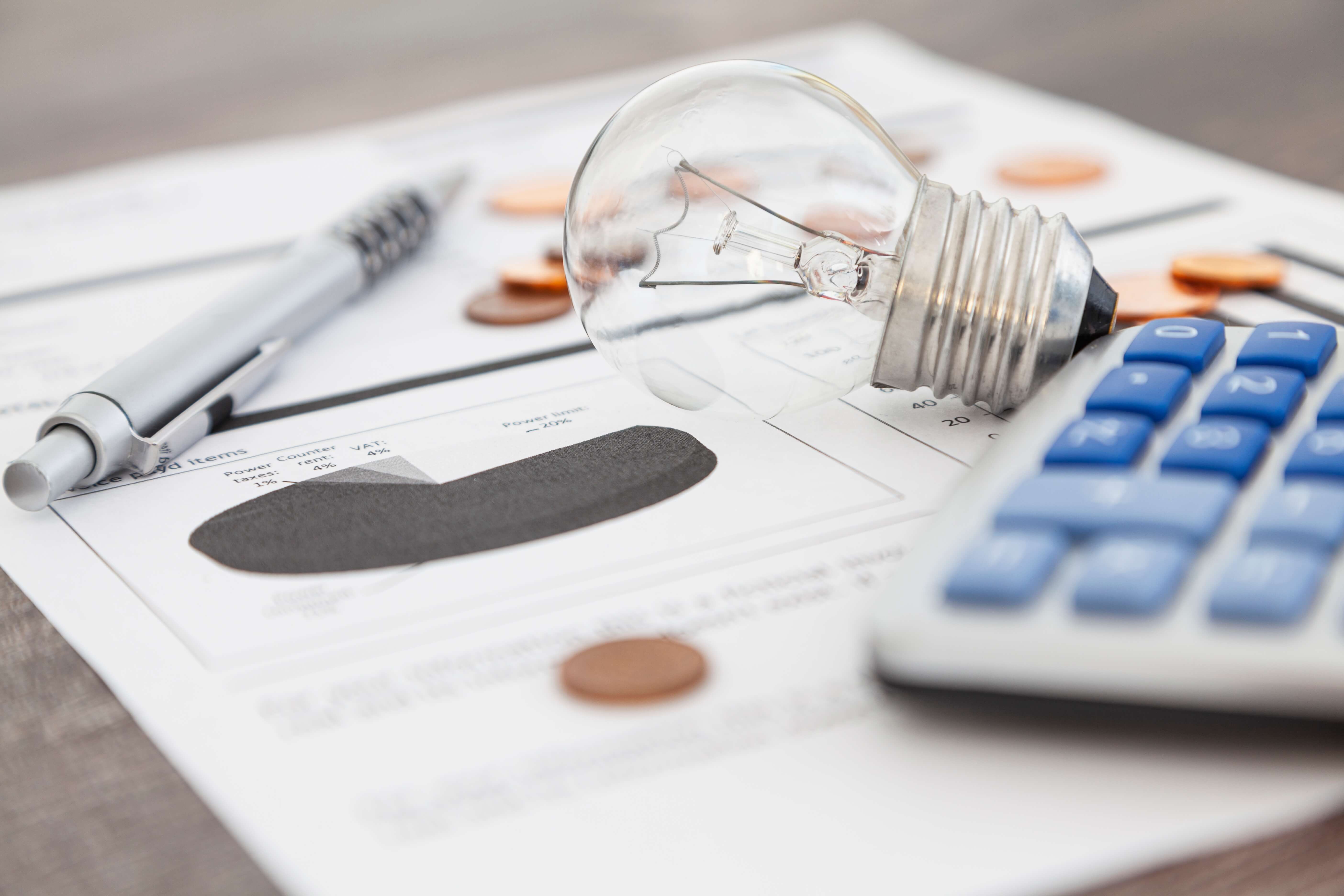lightbulb coin calculator with blue buttons and a silver pen lying on a document on a table lightbulb coin calculator with blue buttons and a silver pen lying on a document on a table