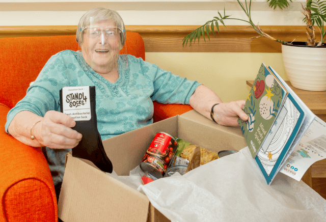 Elderly lady opening a care box filled with socks, can and books Elderly lady opening a care box filled with socks, can and books