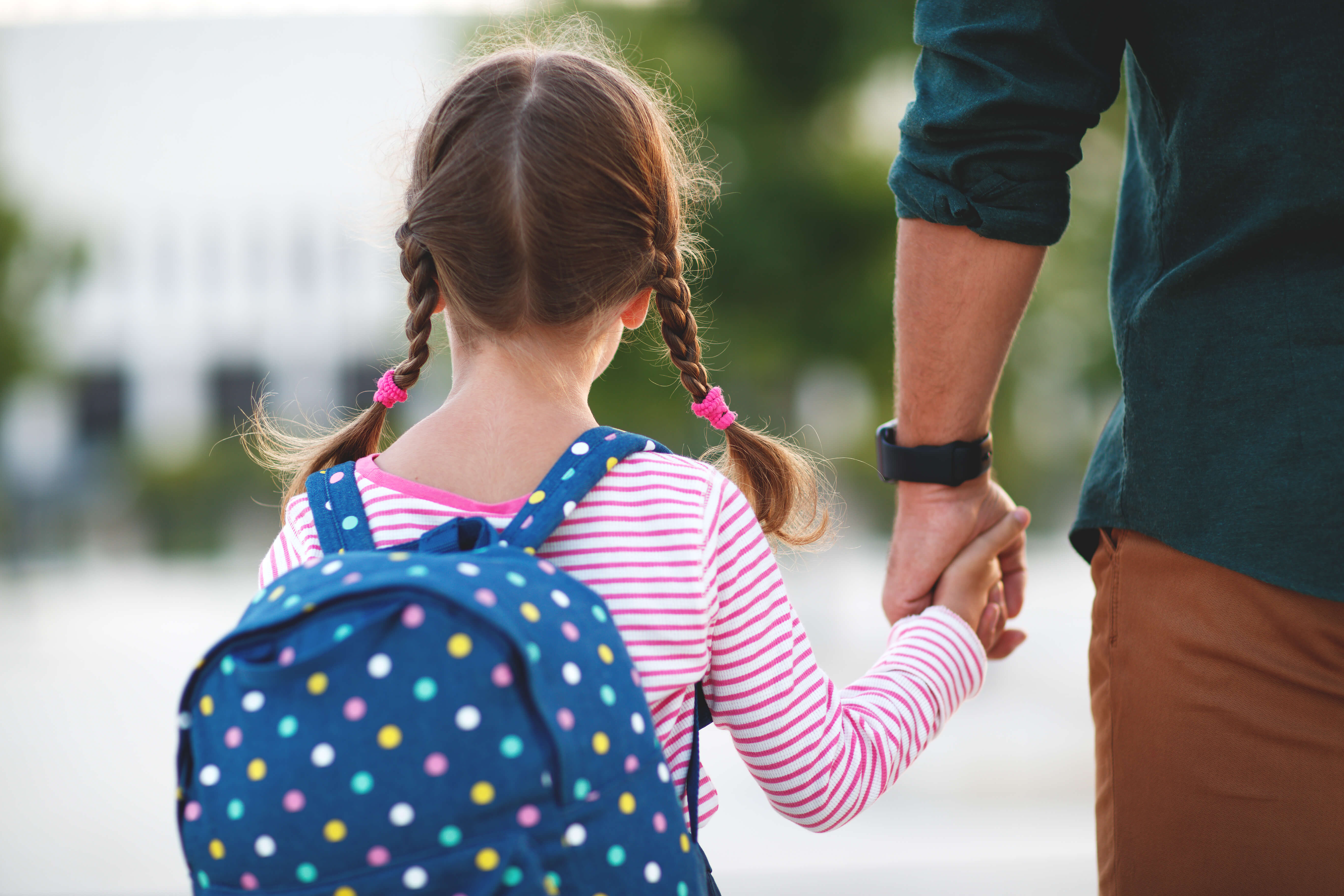 Girl in pigtails carrying a school backpack holding her fathers hand